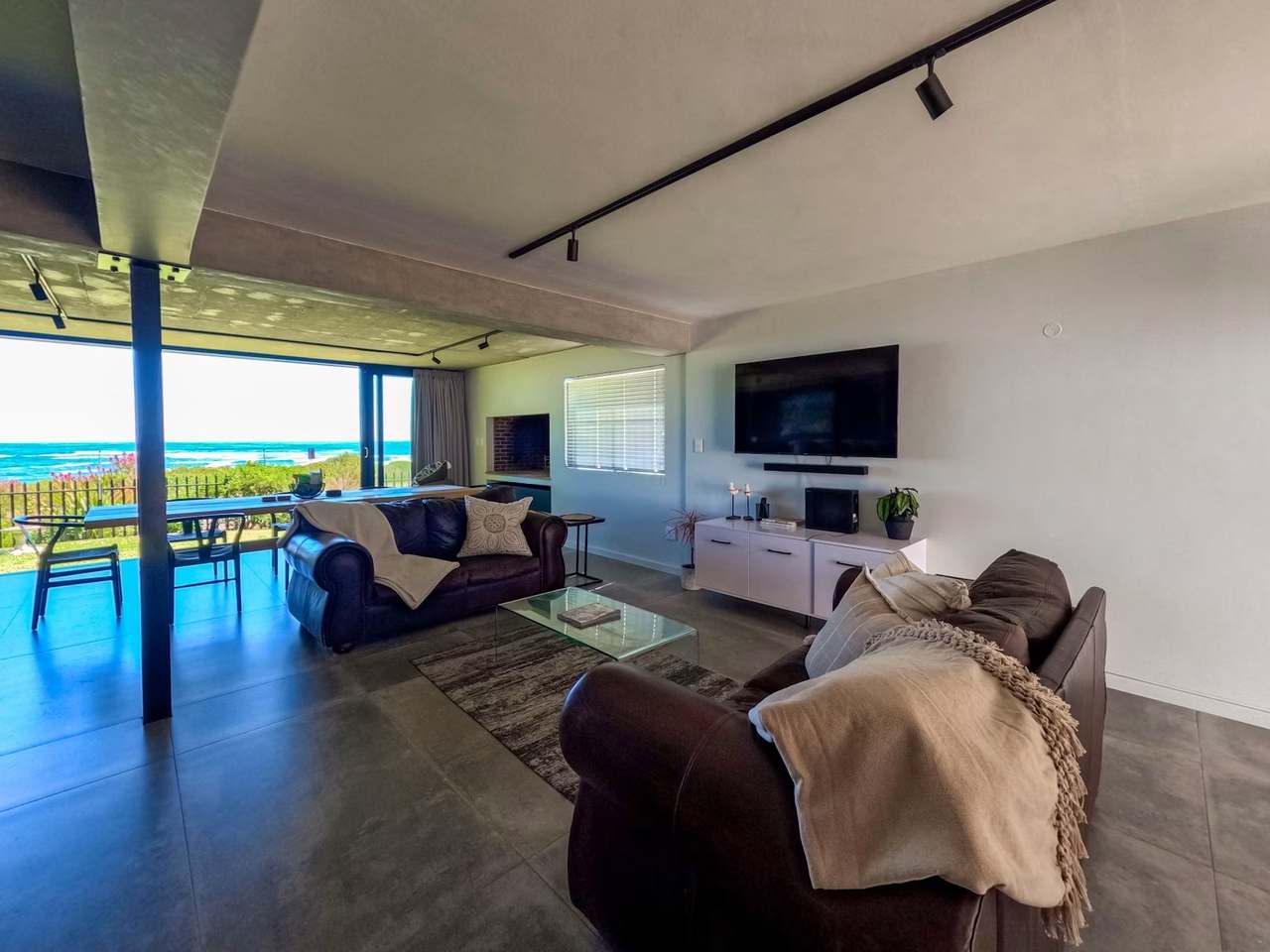 Open-plan lounge at Imoyo Ocean Villa with leather sofas, TV and panoramic Sandbaai sea view